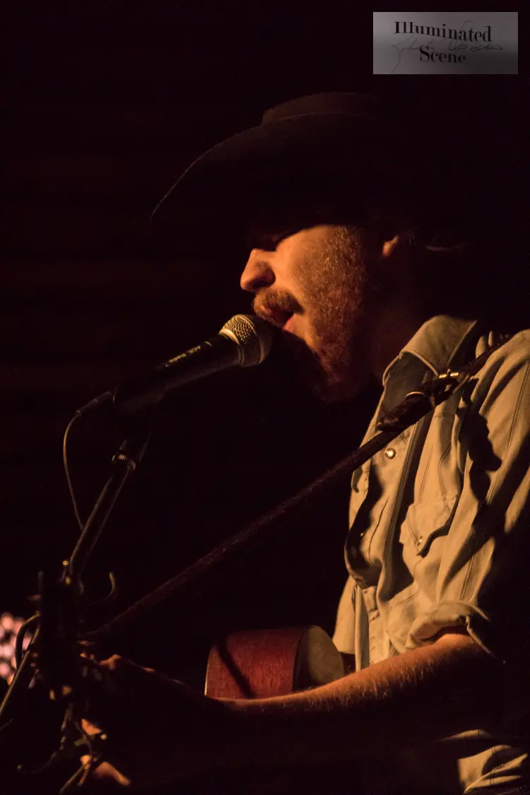 Colter Wall in a black cowboy hat singing into a microphone and playing guitar in 2018.